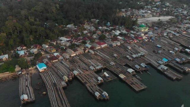 Aerial view of a serene fishing village with boats and docks by the sea at sunset, Tanjung Binga, Indonesia.