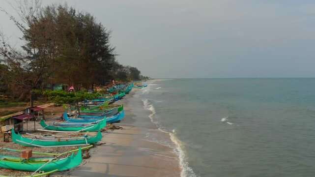Aerial view of serene serdang beach with traditional fishing boats and lush trees, Manggar, Indonesia.