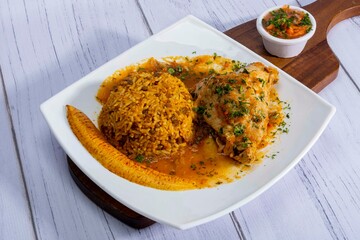 A vibrant, traditional Ecuadorian dish, Seco de Pollo, served with flavorful yellow rice and fried plantains. The dish features a tender chicken leg simmered in a rich, aromatic sauce made from tomato