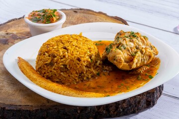 A vibrant, traditional Ecuadorian dish, Seco de Pollo, served with flavorful yellow rice and fried plantains. The dish features a tender chicken leg simmered in a rich, aromatic sauce made from tomato