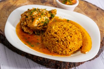 A vibrant, traditional Ecuadorian dish, Seco de Pollo, served with flavorful yellow rice and fried plantains. The dish features a tender chicken leg simmered in a rich, aromatic sauce made from tomato