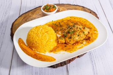 A vibrant, traditional Ecuadorian dish, Seco de Pollo, served with flavorful yellow rice and fried plantains. The dish features a tender chicken leg simmered in a rich, aromatic sauce made from tomato