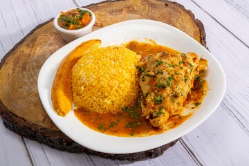 A vibrant, traditional Ecuadorian dish, Seco de Pollo, served with flavorful yellow rice and fried plantains. The dish features a tender chicken leg simmered in a rich, aromatic sauce made from tomato