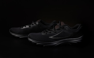 A pair of black sneakers on a black background. Beautiful black sneakers.