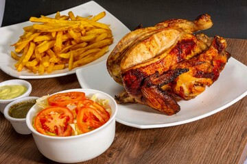 Deliciously charred and smoky Pollo a la Brasa (grilled chicken) served whole and in pieces, accompanied by crispy fries, fresh salad, and a flavorful dipping sauce. A classic Latin American dish, coo