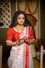 Portrait of young woman, dressed in traditional saree, adorned with gold jewellery, delicately...