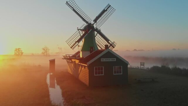 Aerial view of de jonge dirk windmill in a serene meadow with fog at sunrise, zaandam, netherlands.