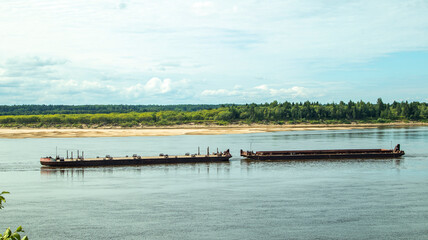 A large river vessel pulls two barges loaded with timber down the river