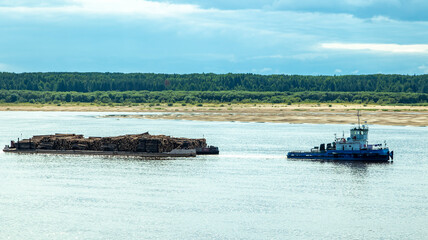 A large river vessel pulls two barges loaded with timber down the river