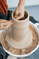 Close-up of a potter's hands making a ceramic vase on a potter's wheel. Vertical photo. 