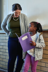 Girl, book and presentation in classroom with teacher, smile and together for development at academy. Child, oral and speech with notebook, education and learning for future with progress at school
