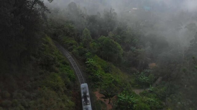 Aerial view of nine arches bridge over train tracks amidst lush tea fields and foggy hills, Ella, Sri Lanka.