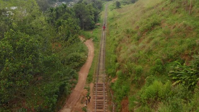 Aerial view of a scenic railway track with people walking through lush greenery and forested hills, Ella, Sri Lanka.
