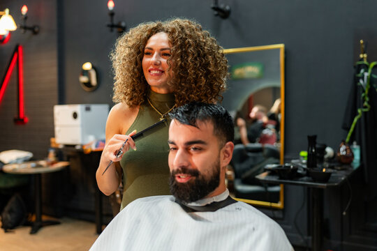 Barber applying styling techniques on a cheerful male customer, creating a fashionable look in a trendy barber shop environment.