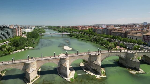 Aerial view of beautiful stone bridge over a river with historic cityscape and greenery, Zaragoza, Spain.