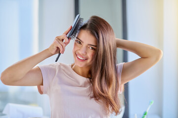 Fototapeta premium Woman, portrait and brushing hair in home, grooming and morning for getting ready in bathroom. Female person, cosmetics tool and hairbrush for hairstyle, Indonesia and treatment for healthy growth