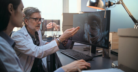 Two diverse scientists discuss 3D visualization of ancient human head anatomy displayed on PC and...