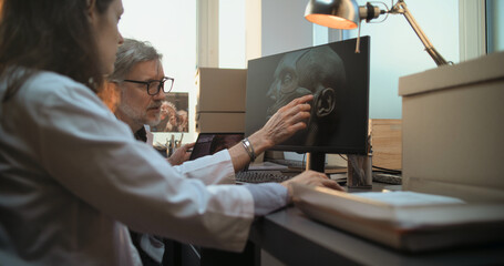 Two diverse scientists discuss 3D visualization of ancient human head anatomy displayed on PC and...