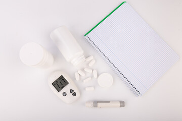 Diabetes Management Tools: Glucose Meter, Notebook, and Pills on White Background