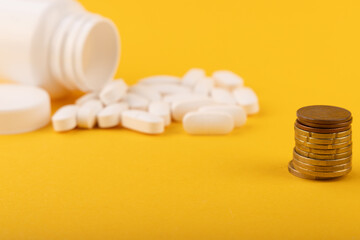 Overturned White Pill Bottle with Pills and Coins on Yellow Background