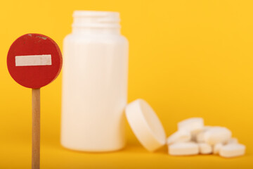 White pill bottle and no entry sign on yellow background, symbolizing caution in the use of...