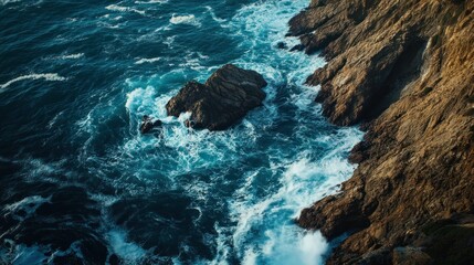 Aerial view of rocky coastline with crashing waves and deep blue ocean.