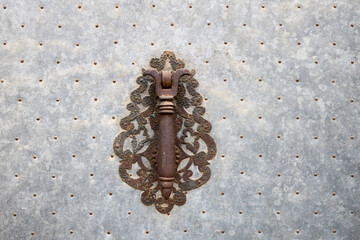 The handle on the metal door in the old style. Old decorative door handle on metal door in ancient building. Doorknocker.