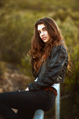 Fototapeta premium Woman, portrait and nature with fashion for style, weekend or outdoor holiday on pole. Young, female person or attractive brunette with stylish clothing, hairstyle or glitter in cool outfit or jacket