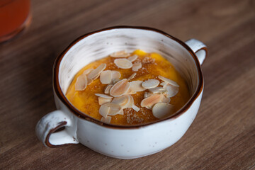 Close-up view of sweat creamy pumpkin crème brûlée dessert (also known as burnt cream or Trinity cream) with almond slices standing on wooden table in restaurant. Soft focus. Desserts theme.