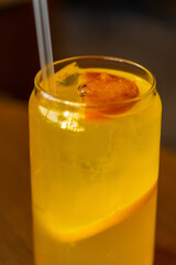 Close-up side view of drinking glass with orange fruit lemonade and drinking straw on wooden table in restaurant or cafe. Soft focus. Cold drinks theme.