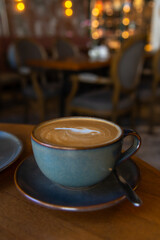 Side view of blue porcelain cup of cappuccino with feather shaped latte art standing on brown wooden table in cafe or restaurant. Soft focus. Copy space. Coffee background. Hot drinks theme.
