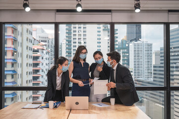 Multiethnic business team wearing face mask during business meeting in modern office. Diverse corporate colleagues brainstorming with technology device