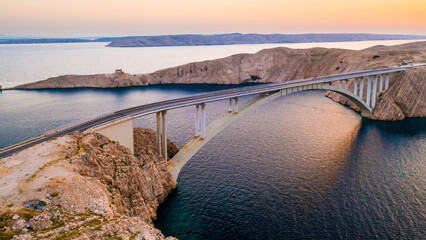 Pag Bridge with driving vehicles over Adriatic Sea channel at sunset. Road network connects island to Croatian mainland offering stunning views