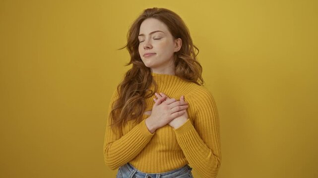 Young caucasian woman wearing sweater standing smiling with hands on chest with closed eyes and grateful gesture on face. health concept. over isolated yellow background