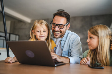 Father and daughters smile and use laptop at home together happy