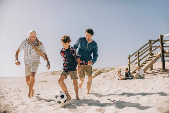 Multi-generational family playing soccer on the beach