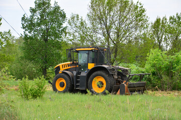 a yellow tractor on the green field with some trees in the background 