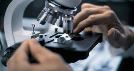 Close up of microbiologist or chemist putting fossil specimen under microscope for analysis. Scientist or archaeologist works with professional equipment in advanced archaeological science laboratory.