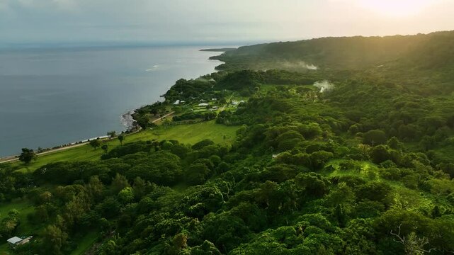 Aerial view of a beautiful tropical coastline with a curvy road surrounded by lush greenery and ocean at sunset, Shefa Province, Vanuatu.