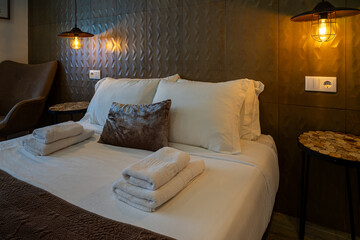 A cozy room with a neatly made bed, fresh folded towels placed on top, and two bedside lamps casting a warm, soft yellow glow. Perfect for a peaceful stay in a local accommodation.