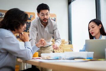 Three people are sitting at a table in a room, talking and working together. Scene is collaborative and focused