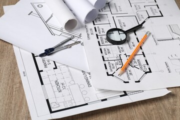 Different engineering drawings, dividers, pencil and magnifying glass on wooden table, closeup