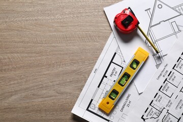 Different engineering drawings, building level and measuring tape on wooden table, flat lay. Space...