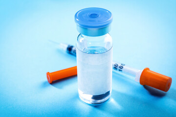 Medication in glass vial and syringe on light blue background, closeup. Space for text