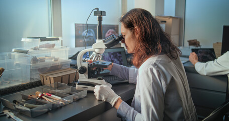 Female chemist or microbiologist conducts fossil analysis under microscope. Bones of ancient human...