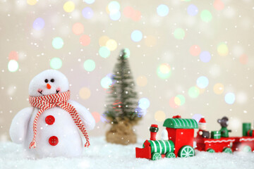 Cute snowman, toy train and small Christmas tree against blurred lights, bokeh effect. Space for text
