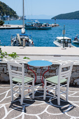 White chairs and a blue table overlooking a sunny harbor in Greece