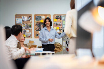 A man is holding a cardboard box and is standing in front of a white board. He is giving a presentation and is holding the box up to show something