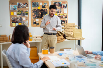 Obraz premium A man is holding a cardboard box and is standing in front of a white board. He is giving a presentation and is holding the box up to show something
