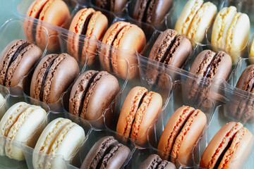 Table top view of a package of a variety of flavored French macarons. White, milk and dark chocolate with orange flavors.